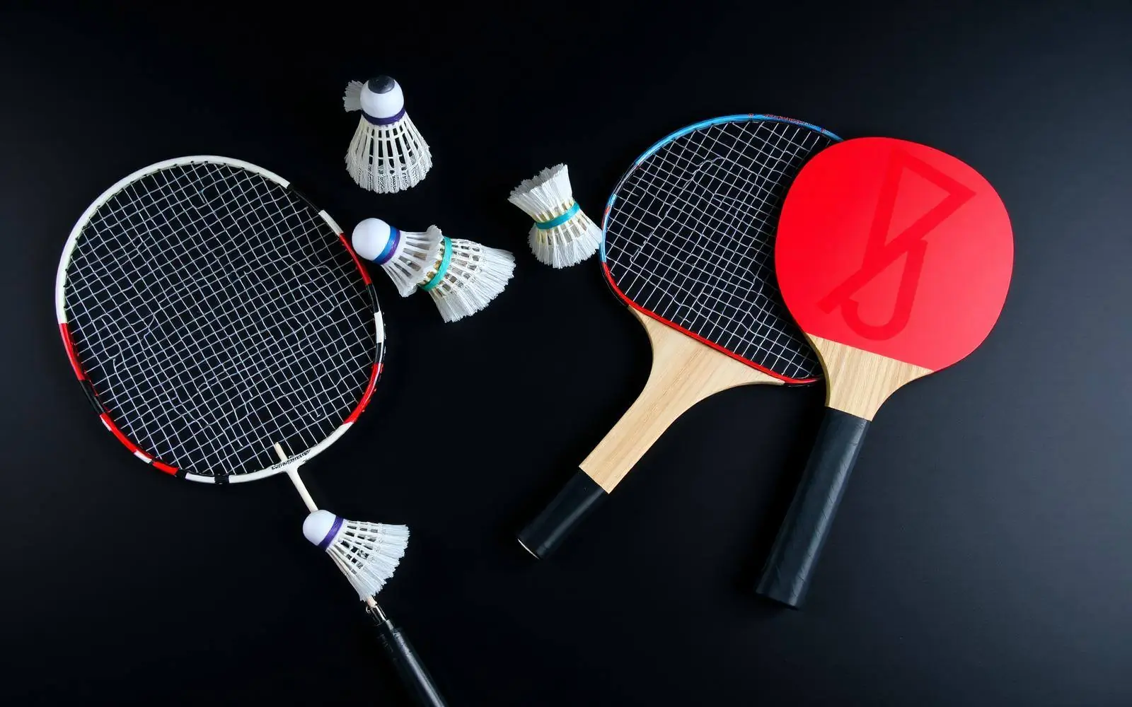 Badminton racquets, shuttlecocks, tennis racquet and table tennis bats on a dark surface